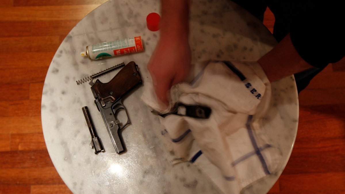 A man checks and cleans his personal army weapon at his house in Zurich.