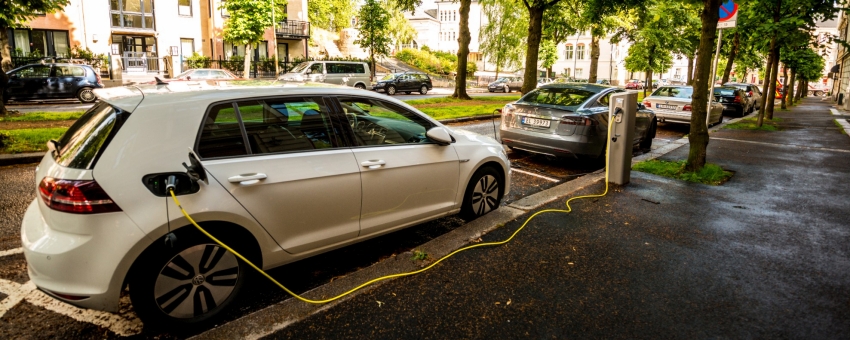 An electric car plugged into a charging station while parked on a residential street.