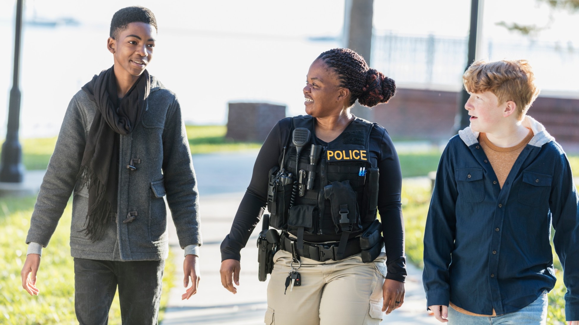A female police officer smiles as she walks with two young teenage boys. Photo by kali9 / Getty Images