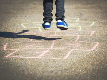 Close up of little boy jumping on a chalk hopscotch outline